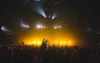 Hands waving in air at music concert with lights behind band on stage